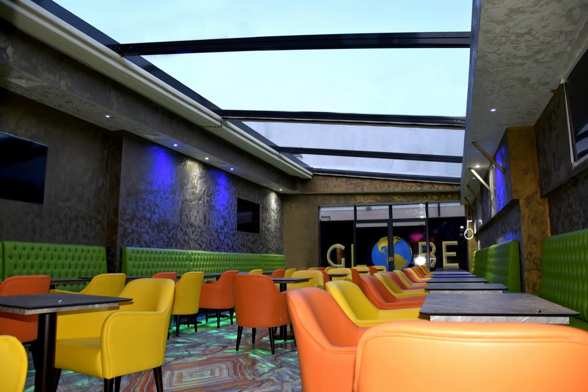The glass-roof terrace at Globe Lounge — rows of green, yellow and orange lounge chairs with the gold GLOBE globe sign at the back