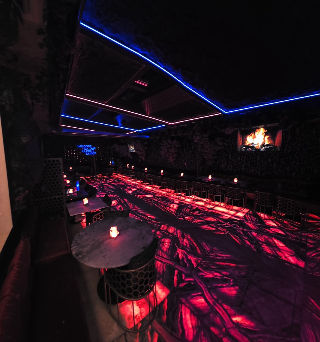 Inside Globe Lounge after dark — blue neon ceiling strips, a glowing red onyx floor and candlelit tables, with a 'Welcome to Globe Lounge' neon sign